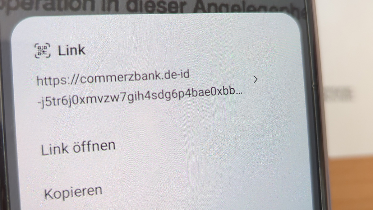 Auf dem Bildschirm eines Smartphones ist die Info eines gescannten QR-Codes zu lesen: https:// commerzbank .de-id-j5tr60xmvzw7gih4sdg6p4bae0cbb...