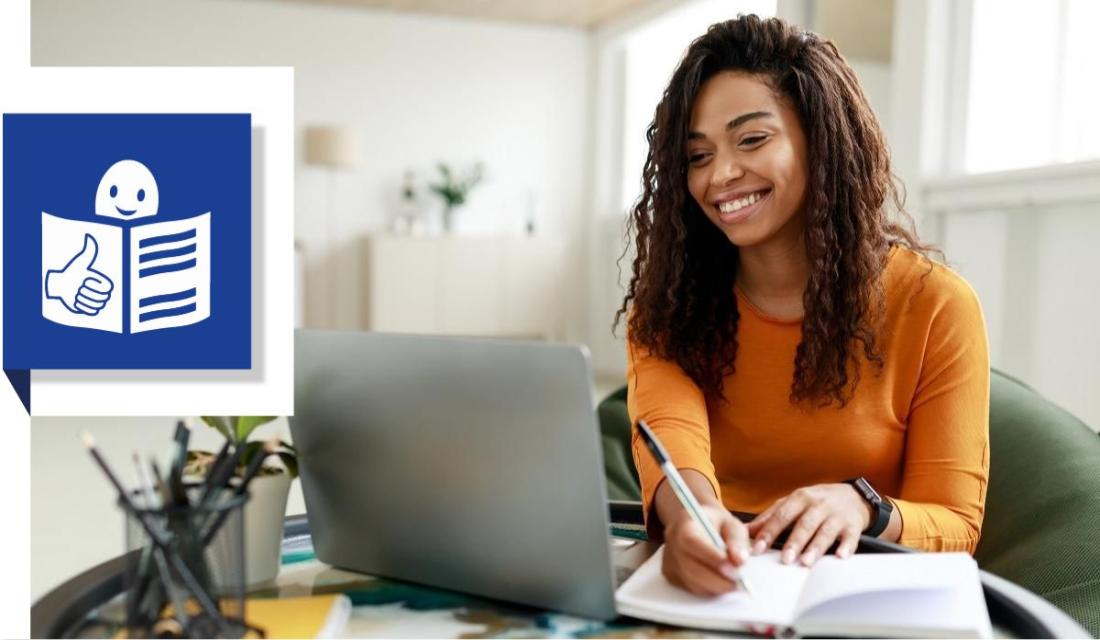 Foto einer Frau, die in einen Laptop-Bildschirm schaut und dabei Notizen in ein Buch macht.