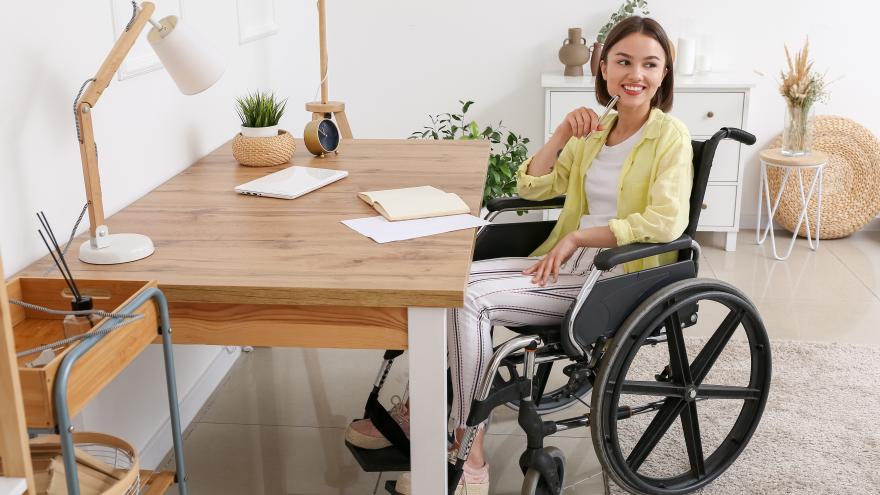 Frau sitzt in einem Rollstuhl am Schreibtisch und lächelt